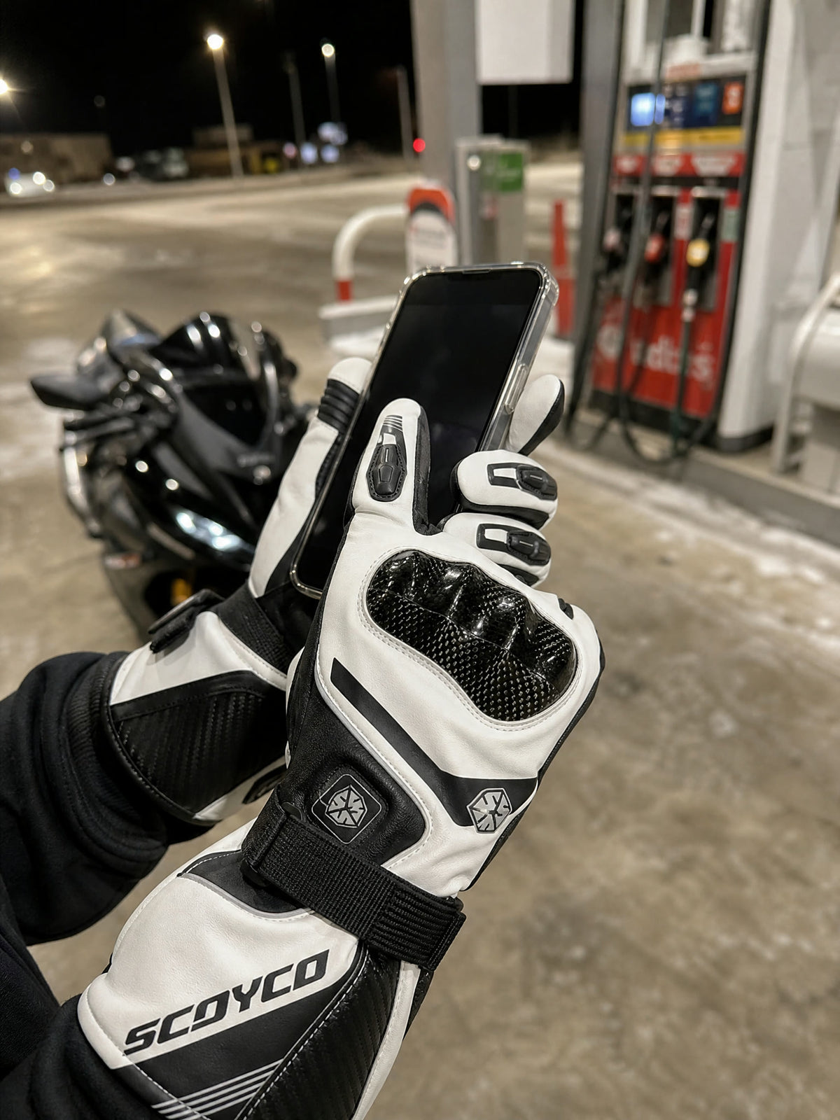 Gloved finger tapping a phone at a gas station at night