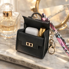 Black mini bag keychain open, holding an earbuds case and a lipstick