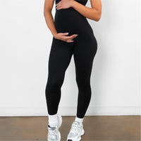 Black over-bump maternity leggings worn with trainers, hands resting on the bump